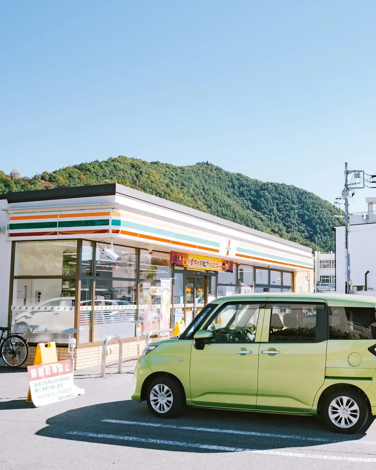 A pale green compact car parked in front of a convenience store